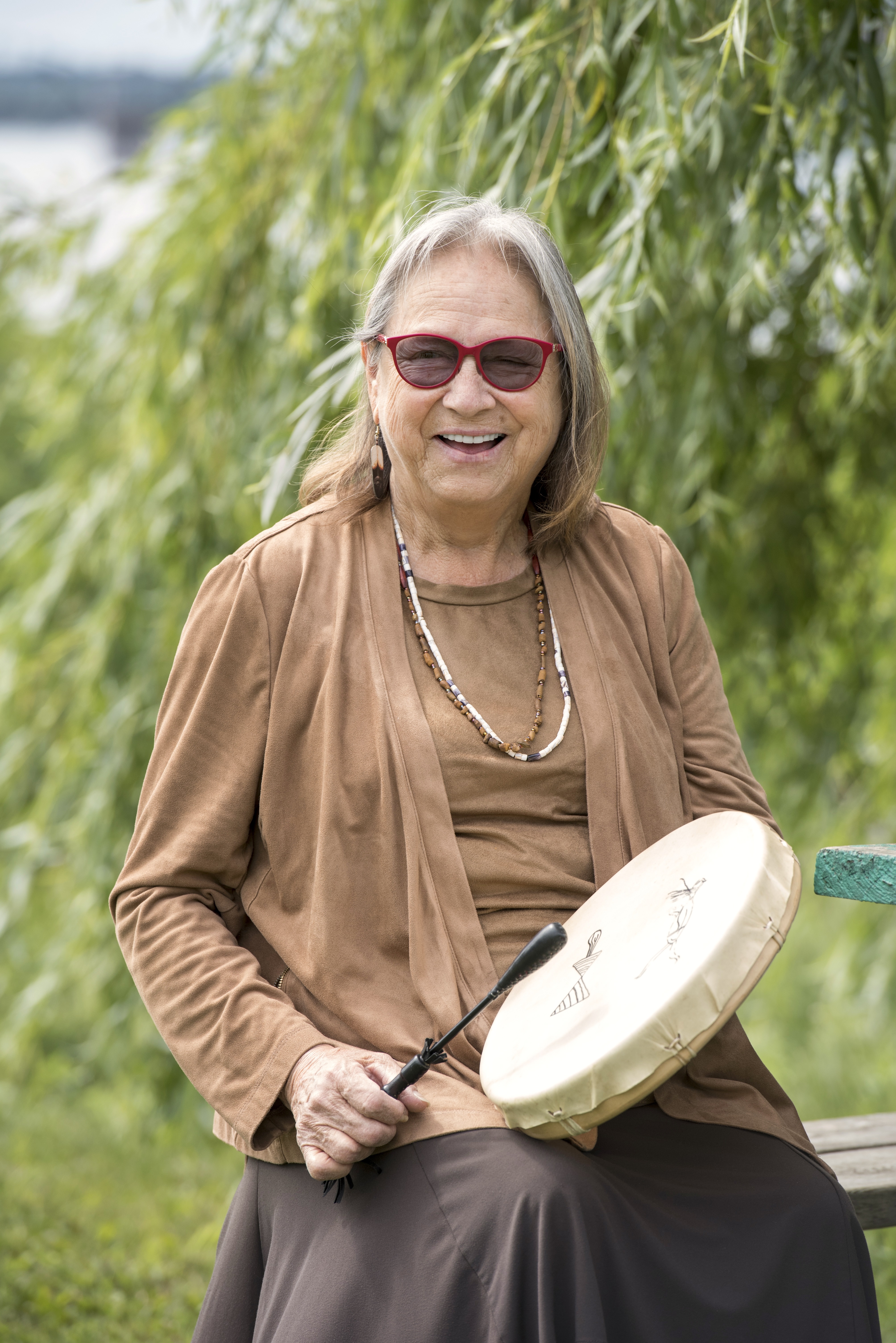 Elder Maggie Paul holding a drum in front of trees