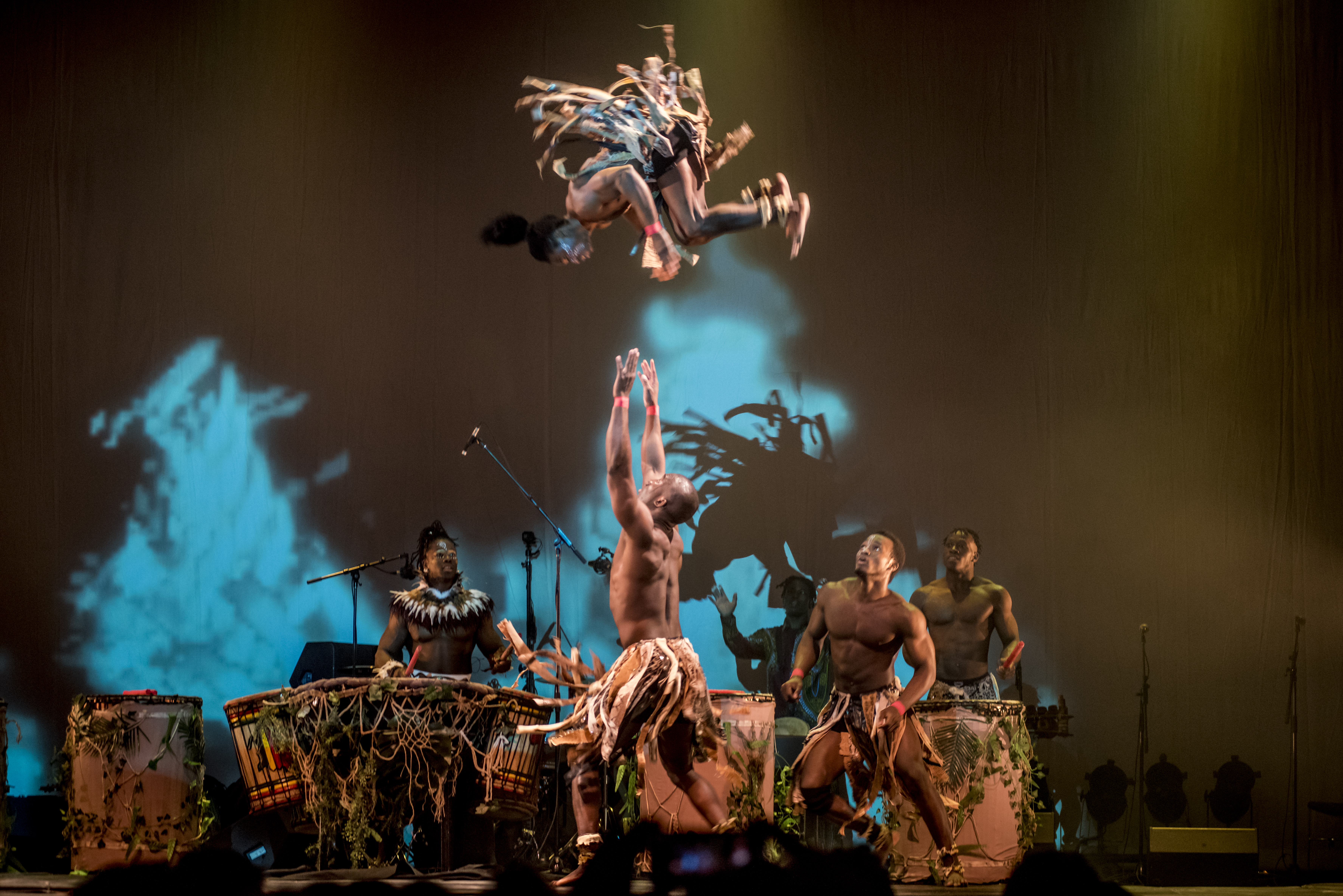 An acrobat flips in the air while others wait to catch them