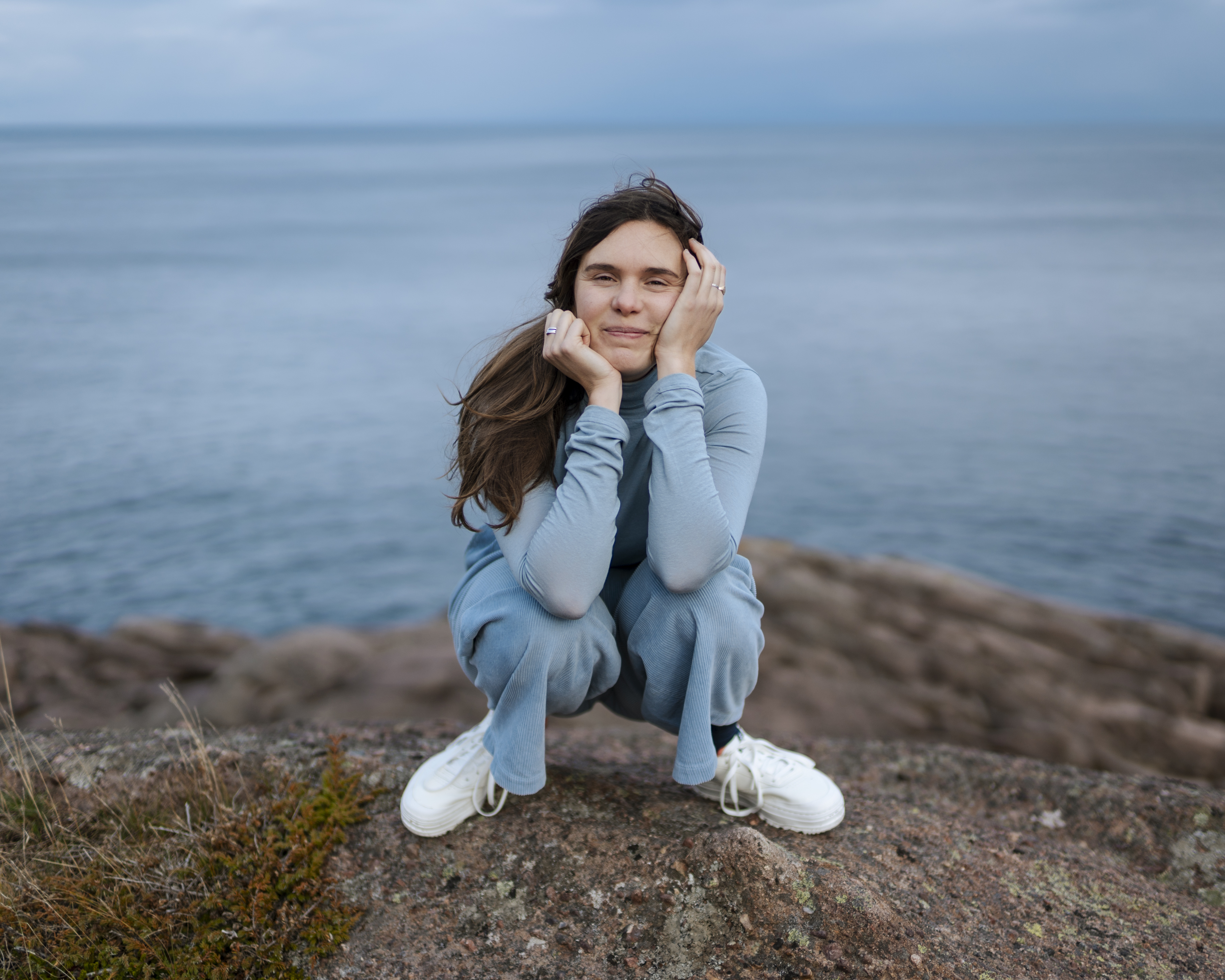 Nico Paulo facing the camera, squatting down on a rock in front of the ocean
