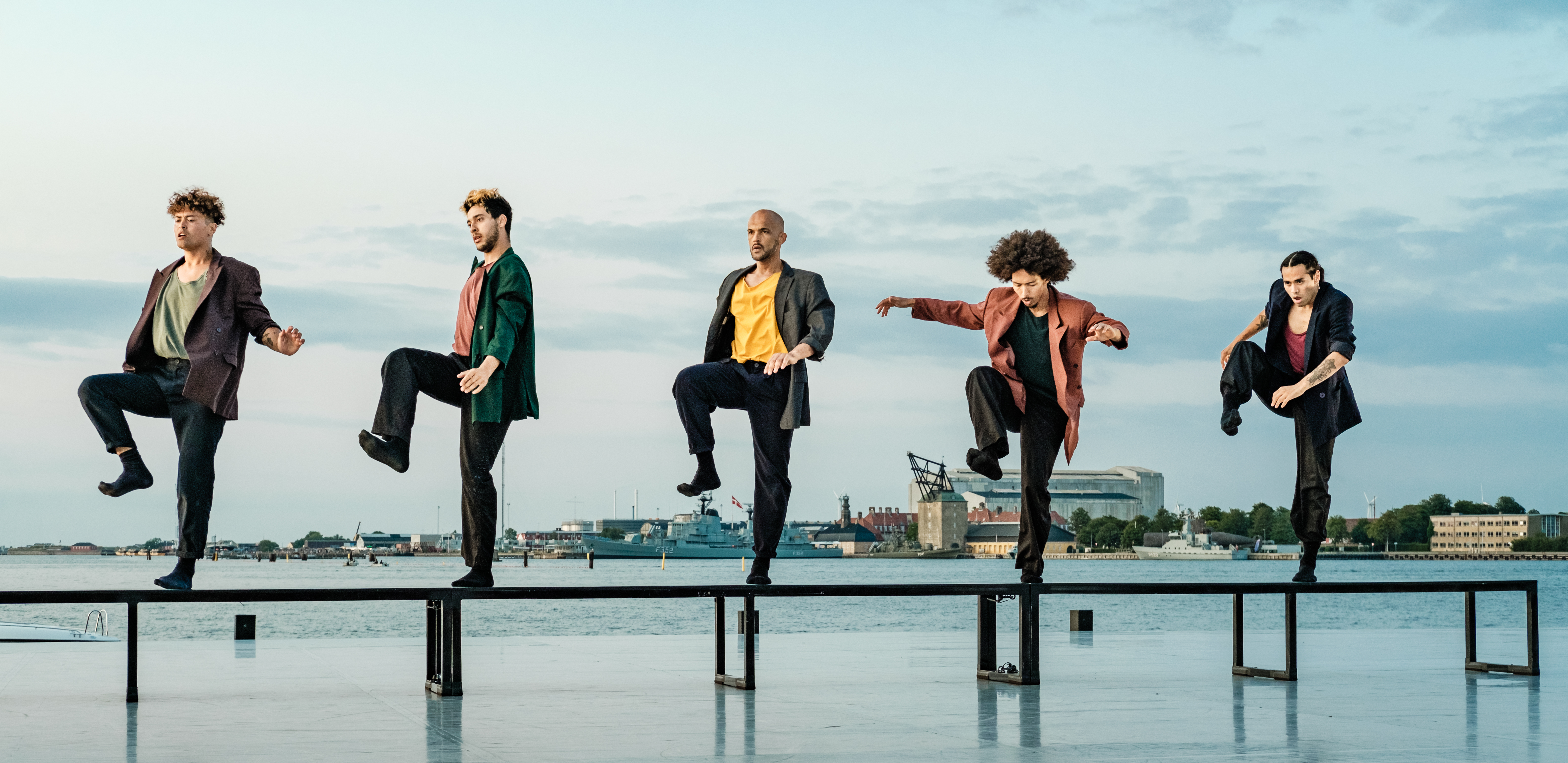 The members of Benched are dancing on a bench on a waterfront