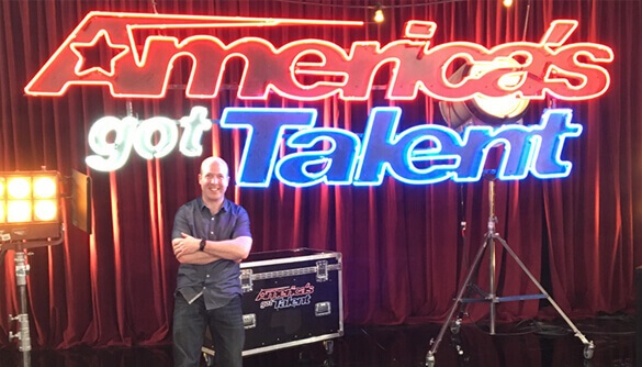 The words America's Got Talent in Neon lit signs with Ian Stewart below the sign.