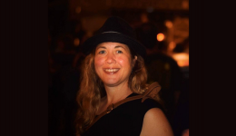 Emma Chevarie in a black hat and shirt in front of a dark, blurred background