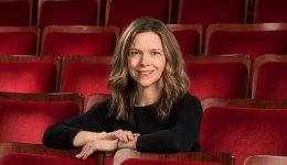 Julie O'Brien in a black shirt sitting in a red theatre seat