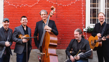 5 bandmembers with instruments in front of a red wall