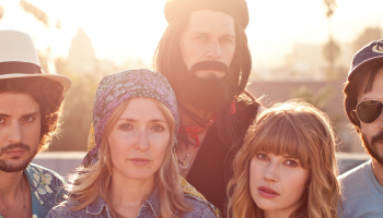 A band photo, 5 people standing together with sun streaming in from behind them.