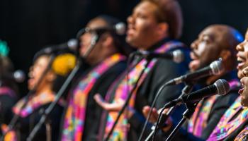 A row of African American singers at microphones for Harlem Gospel Choir