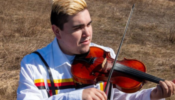 Morgan Toney playing a fiddle standing against a grassy background