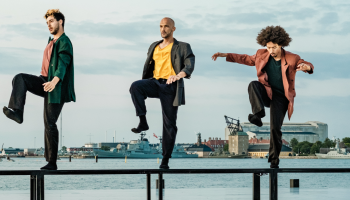 5 dancers standing on one long bench each with one knee up