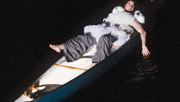 Jeremy Dutcher laying in a canoe, brightly lit against a black background
