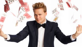 A magician with his arms extended, cards flying in an arc from his hands