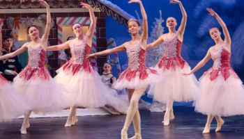 Ballerinas dancing on stage, with the Nutcracker set in the background.