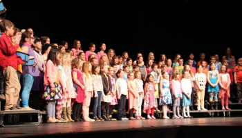 An image of a school choir on stage with a black background.