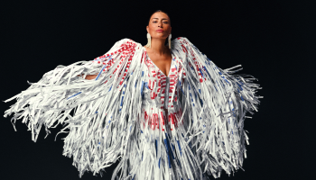 Elisapie in a white Indigenous ribbon dress, arms outstretched with the sleeves flowing around her