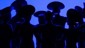 Dancers stand in shadows against a blue background.