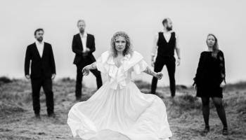 The members of the band stand on a cliffside facing the camera