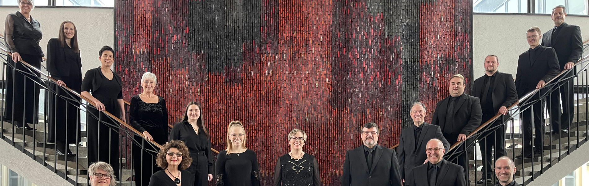 Orchestra members standing on a stairway and in a foyer dressed in black.