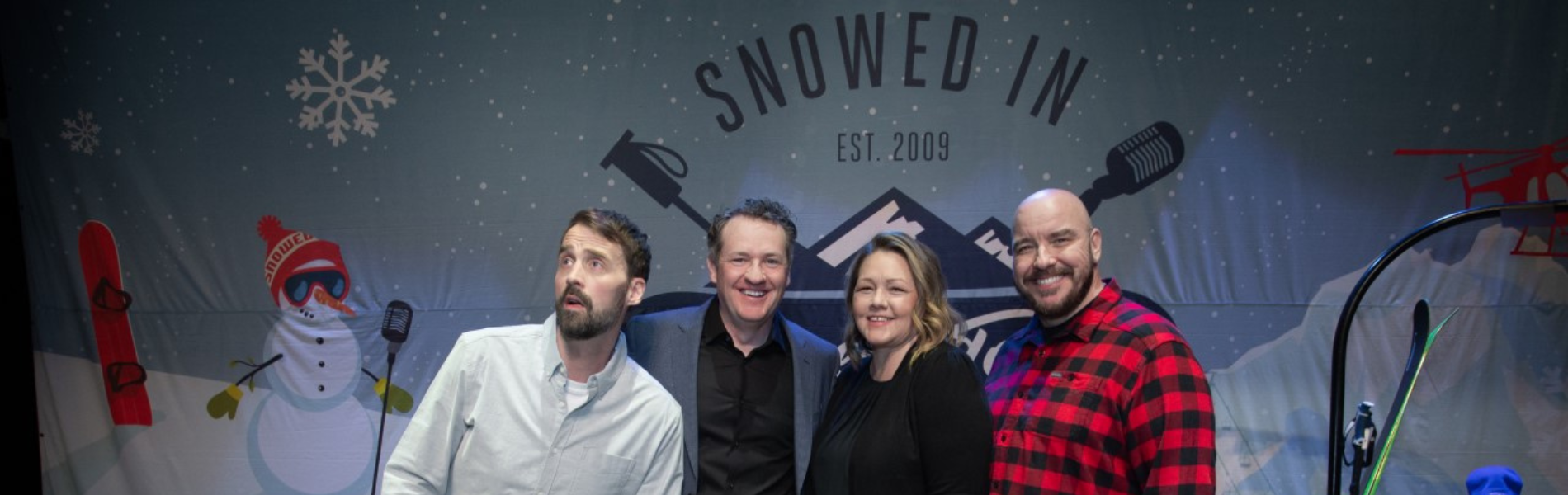 Four comedians standing on stage with the Snowed In Comedy Tour backdrop behind them.