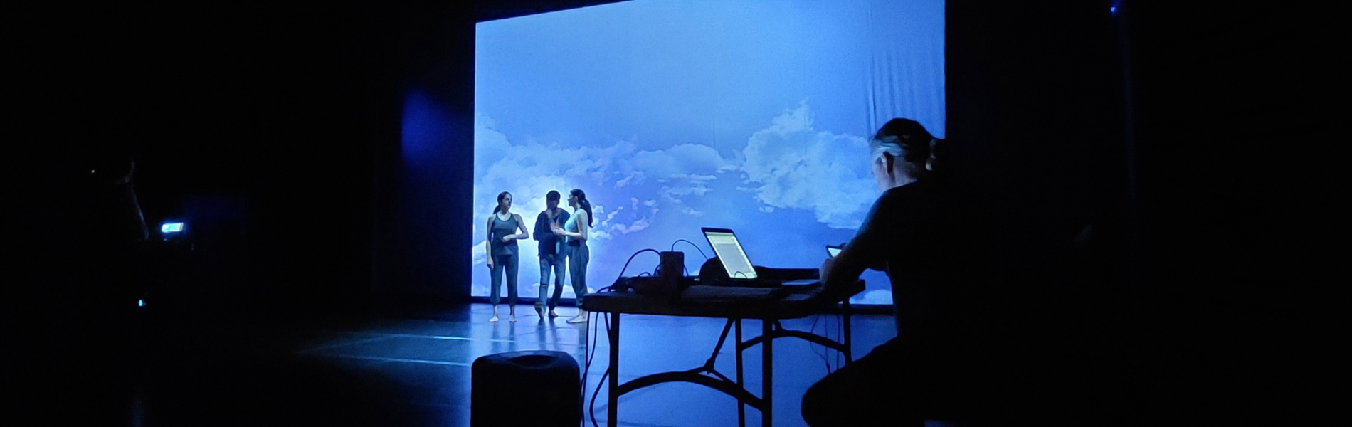 actors on stage with a blue background, a person with a laptop in the foreground