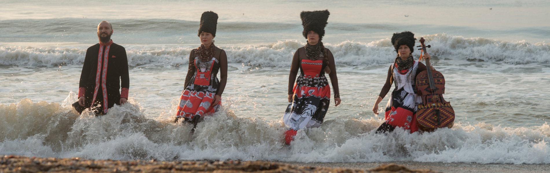4 musicians wearing black and red standing in a wave on the beach