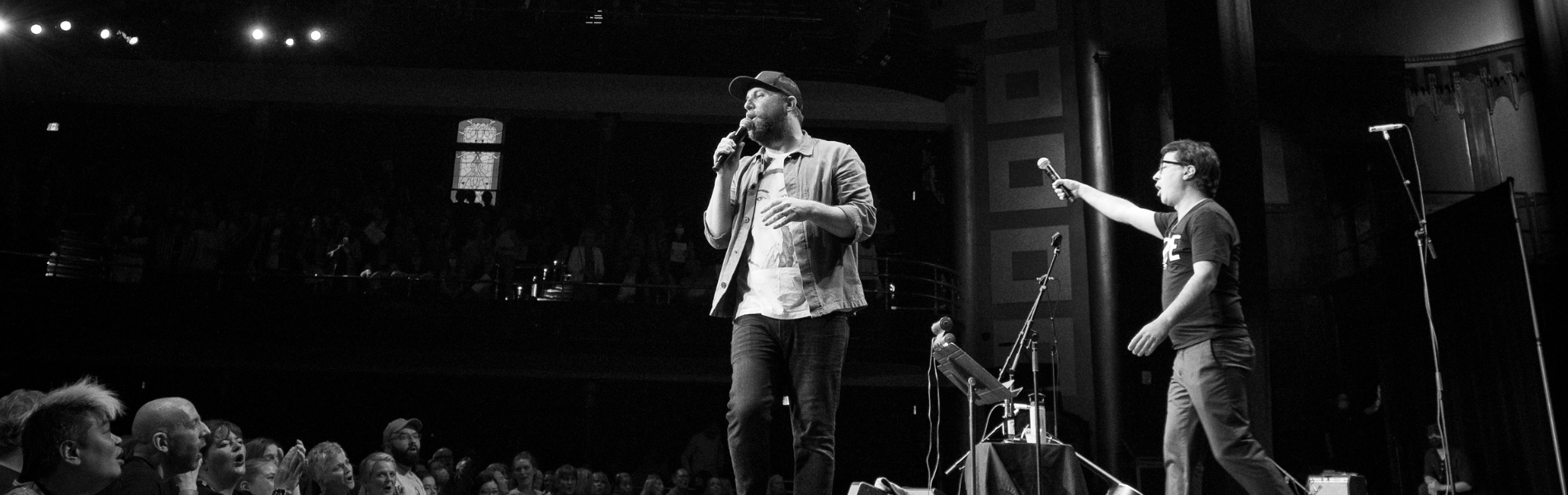 Black & white photo of two members of Choir! Choir! Choir! on stage at a large theatre