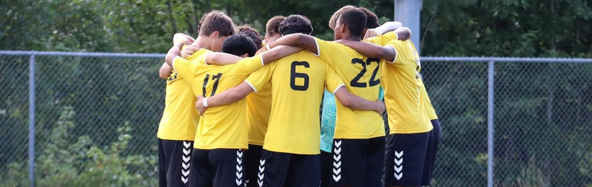 Young soccer players huddled with their arms around each other wearing their yellow jerseys. 