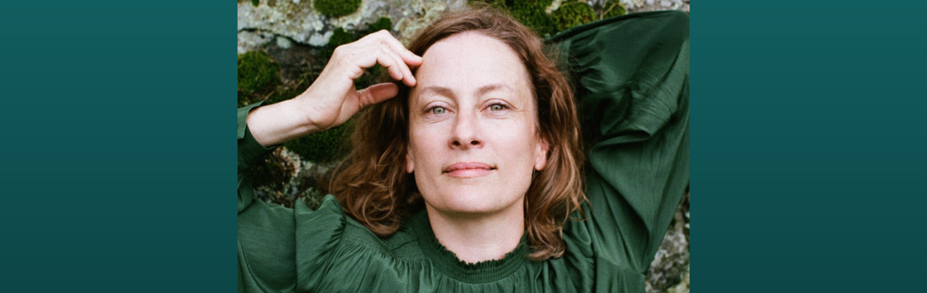 An image of Sarah Harmer in a green shirt with greenery as the back drop.