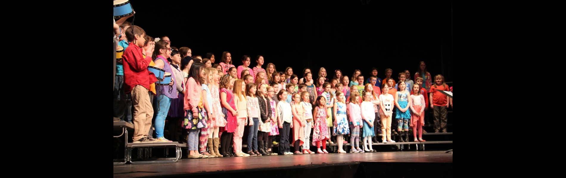 An image of a school choir on stage with a black background.