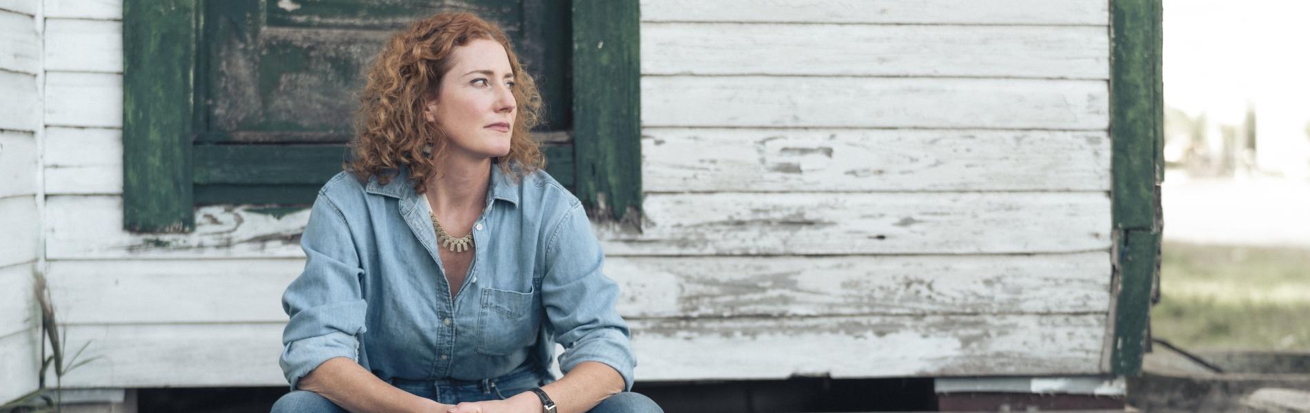 Kathleen Edwards sits outside of an old home looking wistfully off camera