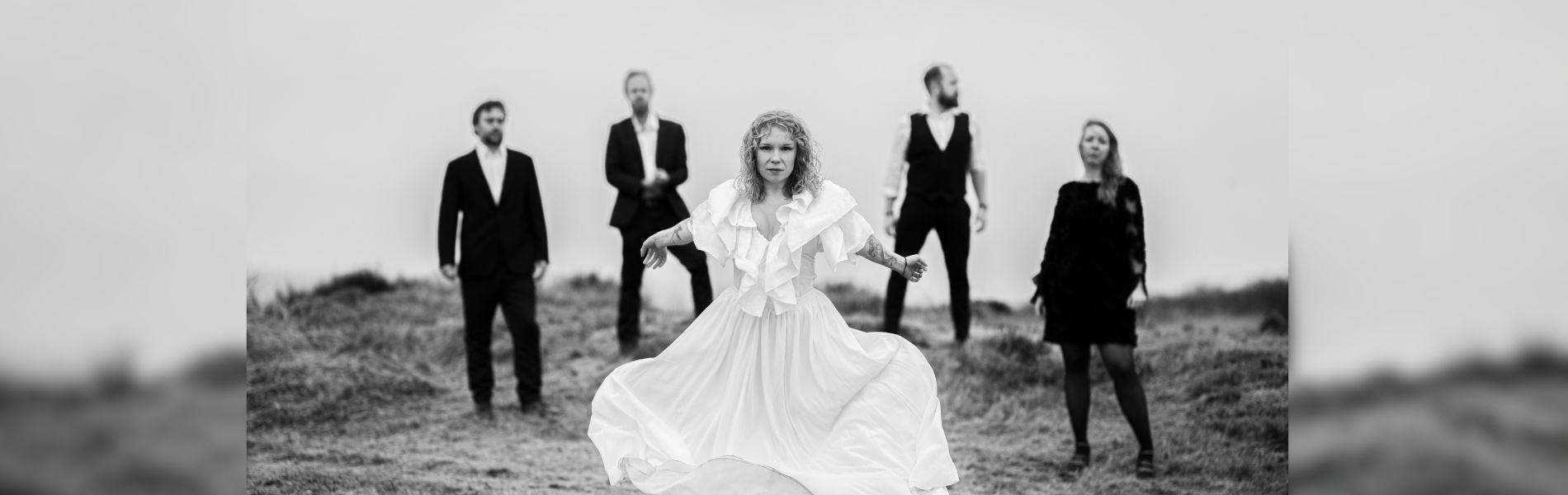 The members of the band stand on a cliffside facing the camera